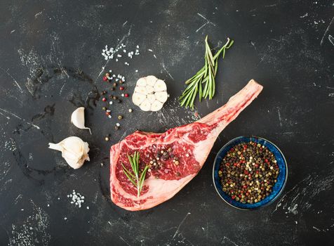 Raw marbled meat steak, herbs, seasonings, garlic, rustic stone background. Beef Rib eye steak on bone, ready for cooking. Top view. Ingredients for meat roasting. Tomahawk steak. Meat steak concept