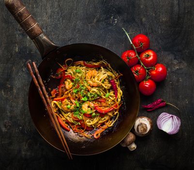 Stir fry noodles in traditional Chinese wok, chopsticks. Asian noodles with vegetables, shrimps. Wok noodles, Chinese dinner/lunch. Black dark background. Top view. Asian/Chinese noodles. Stir frying