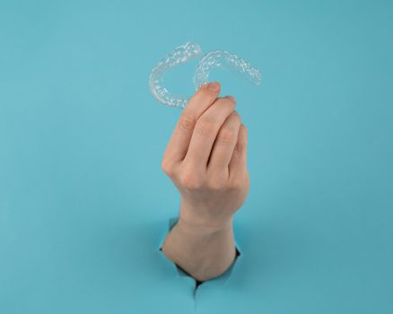 A female hand sticking out of a hole from a blue background holds removable night retainers