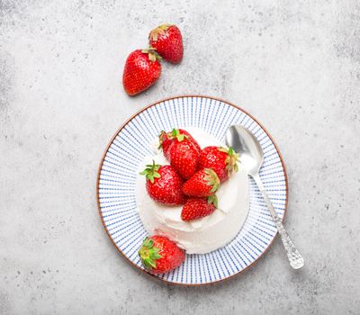 Top-view of fresh Italian cheese ricotta with strawberries on a plate with a spoon, grey rustic stone background, light summer dessert or snack, good for diet or healthy eating. Close-up