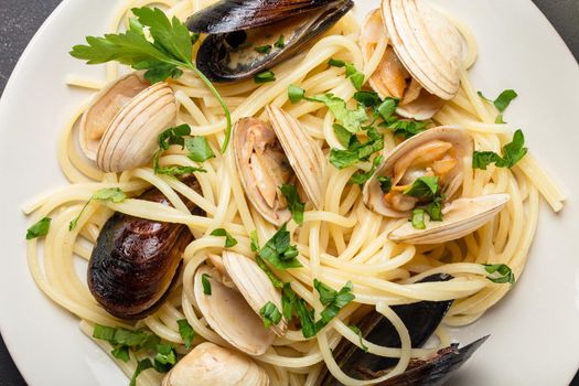 Close-up of spaghetti vongole, Italian seafood pasta with clams and mussels, in plate with herbs on rustic stone background. Traditional Italian sea cuisine, top view