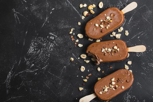 Milk chocolate popsicles with hazelnuts. Close-up. Ice cream popsicles covered with chocolate, sticks, black stone marble background. Space for text. Top view. Chocolate ice cream bars, nuts. Dessert