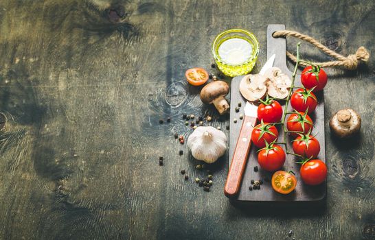 Cherry tomatoes, mushrooms on wooden cutting board, knife. With garlic, olive oil. Cooking background. Space for text. Raw ingredients for cooking. Cooking dinner. Selective focus. Food background