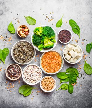 Top view of different vegan protein sources: beans, lentils, quinoa, tofu, vegetables, spinach, nuts, chickpeas, rice, stone rustic background. Healthy balanced vegetarian nutrition for vegans