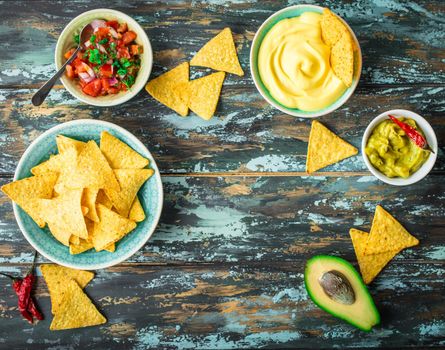 Mexican tortilla chips with guacamole, cheese, salsa dips. Space for text. Mexican party food, appetizers. Top view. Tortilla chips, assorted sauces, hot pepper, avocado, rustic wooden background