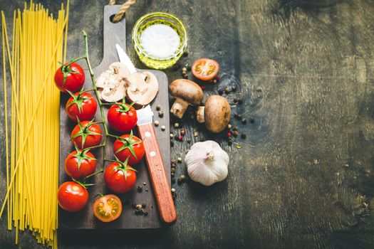 Cherry tomatoes, mushrooms, spaghetti, wooden cutting board, knife. Garlic, olive oil. Cooking background. Space for text. Ingredients for cooking. Cooking dinner. Selective focus. Food background