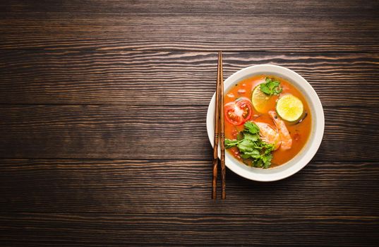 Hot fresh spicy traditional Thai soup tom yum with shrimps in a bowl on rustic wooden background with space for text, top view. Authentic sweat and sour asian soup popular in Southeast Asia