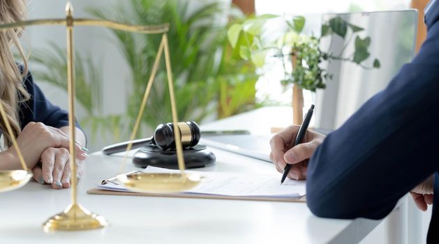 Justice and Law concept. Legal counsel presents to the client a signed contract with gavel and legal law or legal having team meeting at law firm in background.