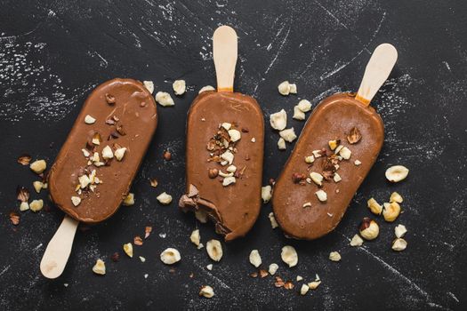 Milk chocolate popsicles with hazelnuts. Close-up. Ice cream popsicles covered with chocolate, sticks, black stone background. Top view. Chocolate ice cream bars, nuts. Dessert. Bitten popsicle