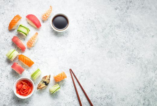 Assorted sushi set on white concrete background. Space for text. Japanese sushi, rolls, soy sauce, ginger, chopsticks. Top view. Sushi nigiri. Japanese dinner/lunch. Food frame. Different sushi mixed