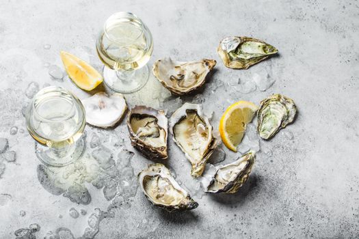 Close-up of half dozen of fresh opened oysters and shells with lemon wedges, two glasses of white wine or champagne, top view, grey rustic concrete background. Romantic or celebration with oysters.