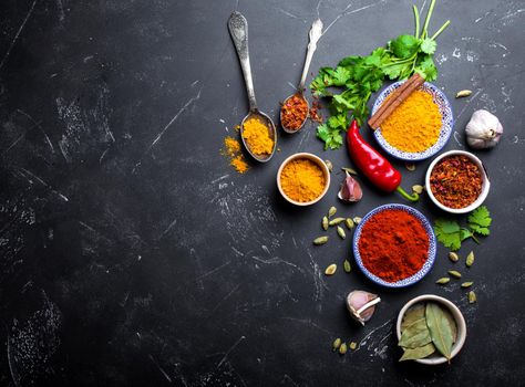 Indian food cooking background. Traditional Indian spices and ingredients. Curry, turmeric, cardamom, garlic, pepper, fresh cilantro, cinnamon. Preparing exotic meal. Top view, space for text