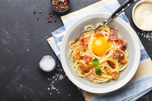 Traditional Italian pasta dish, spaghetti carbonara with yolk, parmesan cheese, bacon in plate on black rustic stone background, top view, space for text. Italian dinner with pasta