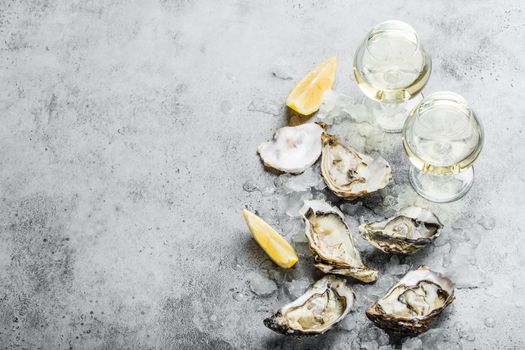 Close-up of half dozen of fresh opened oysters and shells with lemon wedges, two glasses of white wine or champagne, top view, grey rustic concrete background, space for text. Romantic or celebration.