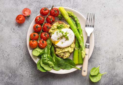 Healthy vegetarian meal plate. Toast, avocado, poached egg, asparagus, baked tomatoes, spinach. Stone background. Vegetarian breakfast plate. Clean healthy eating. Diet. Organic healthy food. Top view