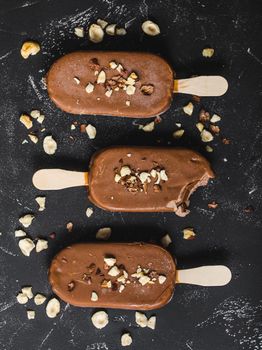 Milk chocolate popsicles with hazelnuts. Close-up. Ice cream popsicles covered with chocolate, sticks, black stone background. Top view. Chocolate ice cream bars, nuts. Dessert. Bitten popsicle