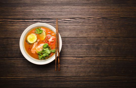 Hot fresh spicy traditional Thai soup tom yum with shrimps in a bowl on rustic wooden background with space for text, top view. Authentic sweat and sour asian soup popular in Southeast Asia