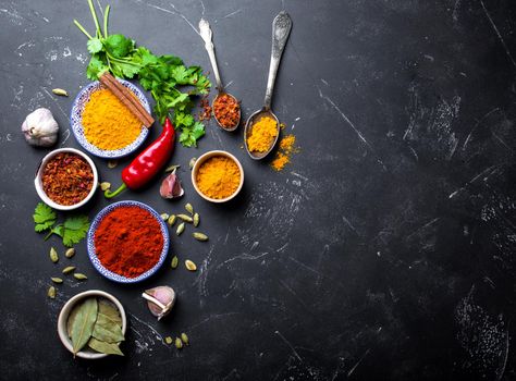 Indian food cooking background. Traditional Indian spices and ingredients. Curry, turmeric, cardamom, garlic, pepper, fresh cilantro, cinnamon. Preparing exotic meal. Top view, space for text