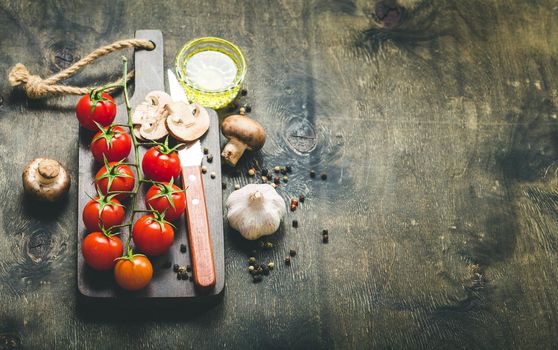 Cherry tomatoes, mushrooms on wooden cutting board, knife. With garlic, olive oil. Cooking background. Space for text. Raw ingredients for cooking. Cooking dinner. Selective focus. Food background