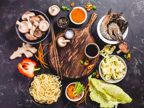 Asian food cooking concept. Empty wooden board, noodles, vegetables stir fry, shrimps, sauces, chopsticks. Asian/Chinese food. Top view. Ingredients for making Asian/Chinese dinner. Chinese noodles