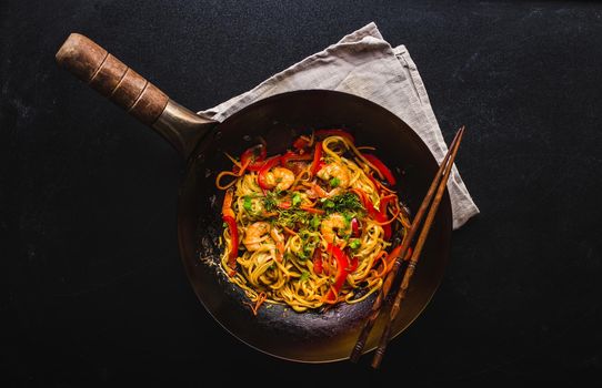 Stir fry noodles in traditional Chinese wok, chopsticks. Asian noodles with vegetables, shrimps. Wok noodles, Chinese dinner/lunch. Black dark background. Top view. Asian/Chinese noodles. Stir frying