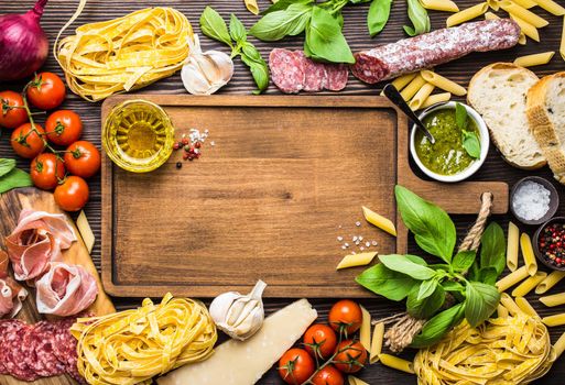 Top view of Italian traditional food, appetizers and snacks as salami, prosciutto, cheese, pesto, ciabatta, olive oil, pasta on rustic wooden board with space for text