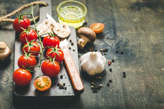 Cherry tomatoes, mushrooms on wooden cutting board, knife. With garlic, olive oil. Cooking background. Space for text. Raw ingredients for cooking. Cooking dinner. Selective focus. Food background