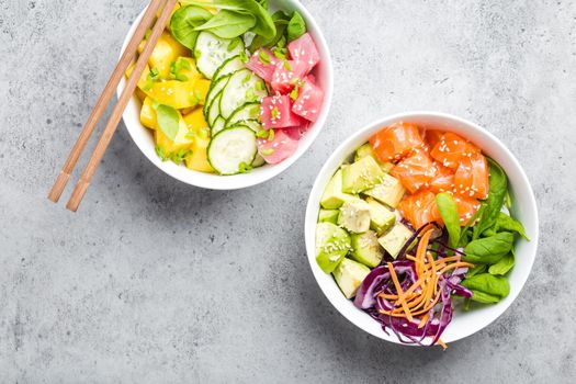 Top view of two assorted poke bowls with fresh raw tuna, salmon, vegetables, fruit. Traditional Hawaiian dish on rustic stone background. Healthy and clean eating concept. Poke with slices of raw fish