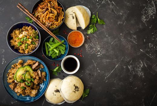 Asian assorted food set, dark rustic stone background. Chinese dishes. Chinese stir-fry noodles, asian rice with meat, dim sum, snacks, steamed Chinese buns. Space for text. Top view. Asian style