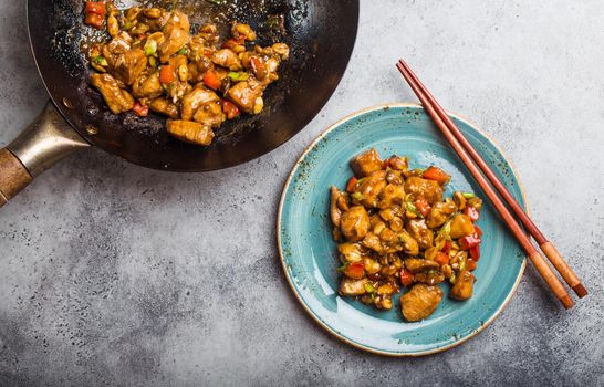 Top view of Kung Pao chicken on a plate ready for eat. Stir-fried Chinese traditional dish with chicken, peanuts, vegetables, chili peppers. Chinese dinner, chopsticks, rustic concrete background