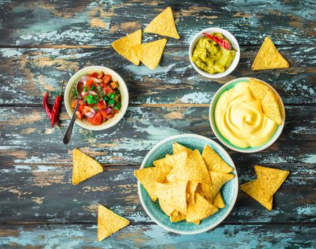 Mexican tortilla chips with guacamole, cheese, salsa dips. Nachos and assorted dips. Mexican party food, appetizers. Top view. Tortilla chips, sauces, hot pepper, avocado, rustic wooden background