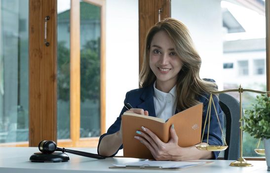 Confident and successful young Asian female lawyer or business legal consultant reading a law book or writing something on her notebook at her office