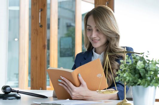 Confident and successful young Asian female lawyer or business legal consultant reading a law book or writing something on her notebook at her office