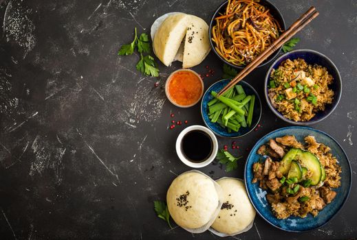 Asian assorted food set, dark rustic stone background. Chinese dishes. Chinese stir-fry noodles, asian rice with meat, dim sum, snacks, steamed Chinese buns. Space for text. Top view. Asian style