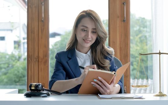 Confident and successful young Asian female lawyer or business legal consultant reading a law book or writing something on her notebook at her office