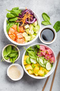 Two assorted poke bowls, raw tuna, salmon, vegetables, fruit. Top view, close-up. Hawaiian dish, rustic stone background. Healthy and clean eating concept. Poke with slices of raw fish, chopsticks