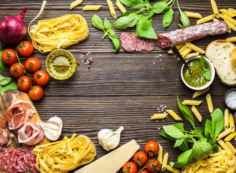 Top view of Italian traditional food, appetizers and snacks as salami, prosciutto, cheese, pesto, ciabatta, olive oil, pasta on rustic wooden background with space for text in centre