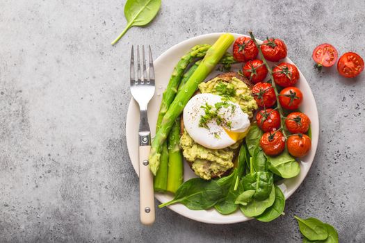 Healthy vegetarian meal plate. Toast, avocado, poached egg, asparagus, baked tomatoes, spinach. Stone background. Vegetarian breakfast plate. Clean healthy eating. Diet. Organic healthy food. Top view