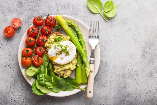 Healthy vegetarian meal plate. Toast, avocado, poached egg, asparagus, baked tomatoes, spinach. Stone background. Space for text. Vegetarian breakfast plate. Diet. Organic clean healthy food. Top view