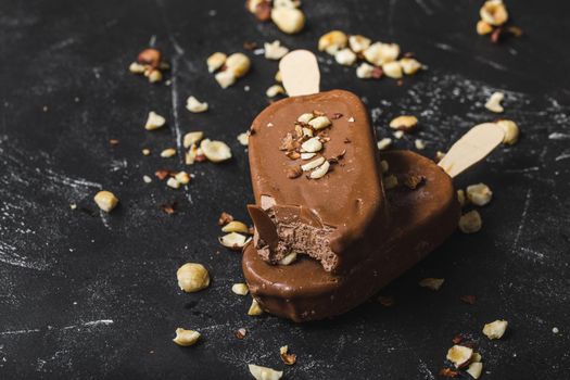 Milk chocolate popsicles with hazelnuts. Close-up. Ice cream popsicles covered with chocolate, sticks, black stone background. Selective focus. Chocolate ice cream bars, nuts. Dessert. Bitten popsicle