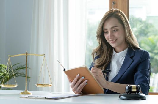 Confident and successful young Asian female lawyer or business legal consultant reading a law book or writing something on her notebook at her office