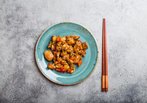 Top view of Kung Pao chicken on a plate ready for eat. Stir-fried Chinese traditional dish with chicken, peanuts, vegetables, chili peppers. Chinese dinner, chopsticks, rustic concrete background