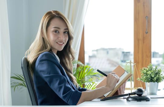 Confident and successful young Asian female lawyer or business legal consultant reading a law book or writing something on her notebook at her office