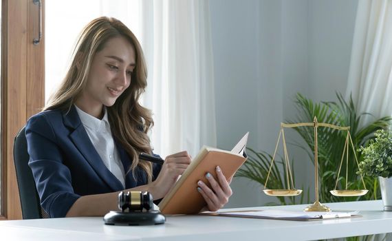 Confident and successful young Asian female lawyer or business legal consultant reading a law book or writing something on her notebook at her office