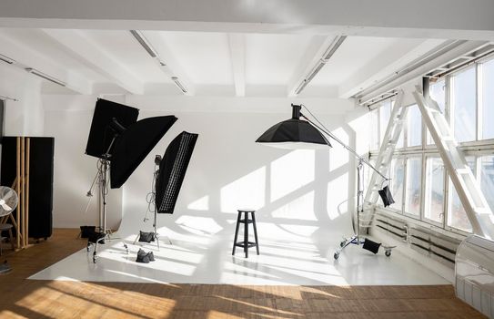 Professional lighting equipment, flashes, c-stands on a cyclorama in modern photo studio with a huge windows. Octabox, stripbox, softbox, buety plate and other stuff for photography