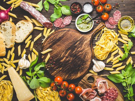 Top view of Italian traditional food, appetizers and snacks as salami, prosciutto, cheese, pesto, ciabatta, olive oil, pasta on rustic wooden round board with space for text in centre and retro style