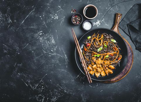 Asian soba noodles, chicken, vegetables, dark background. Space for text. Soba noodles, teriyaki sauce chicken, vegetables, sesame, chopsticks. Asian style dinner. Chinese/Japanese noodles. Top view