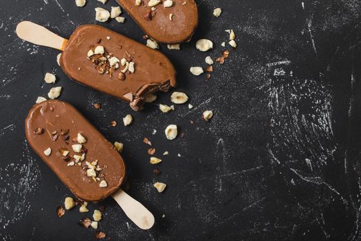 Milk chocolate popsicles with hazelnuts. Close-up. Ice cream popsicles covered with chocolate, sticks, black stone marble background. Space for text. Top view. Chocolate ice cream bars, nuts. Dessert