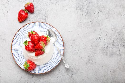 Top view of fresh Italian cheese ricotta with strawberries on a plate with a spoon, grey rustic stone background, light summer dessert or snack, good for diet or healthy eating, with space for text