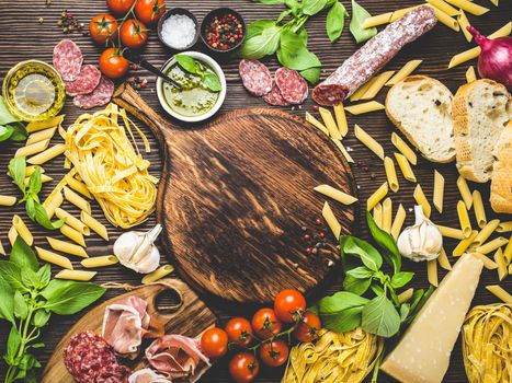 Top view of Italian traditional food, appetizers and snacks as salami, prosciutto, cheese, pesto, ciabatta, olive oil, pasta on rustic wooden round board with space for text in centre and retro style